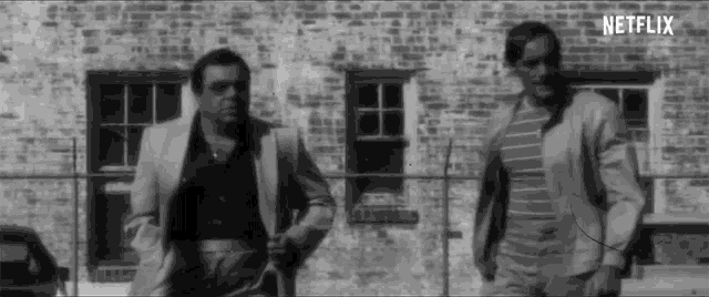 two men are standing in front of a brick building with netflix written in the corner