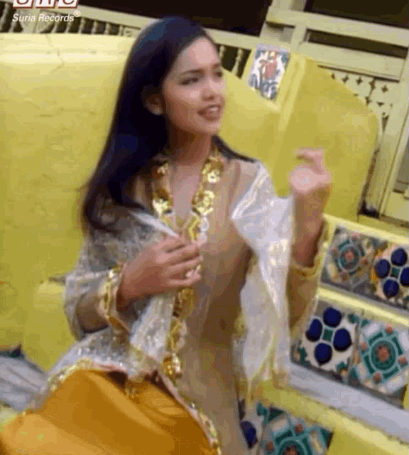 a woman in a gold and white dress is sitting on a yellow bench .