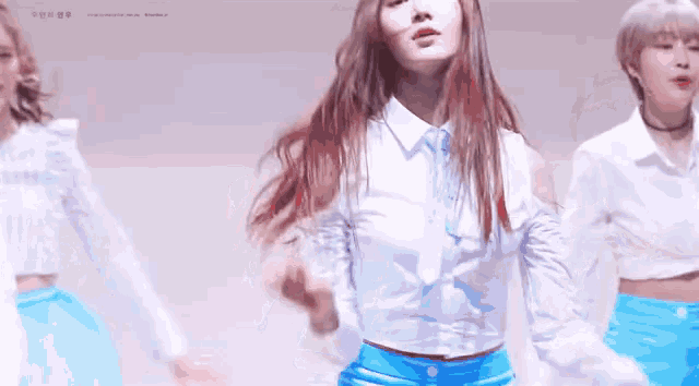 a woman in a white shirt and blue shorts is dancing with two other women in blue skirts .