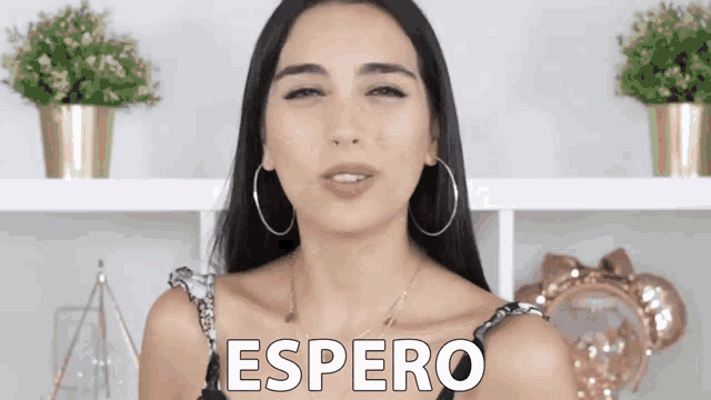 a woman wearing hoop earrings stands in front of a sign that says " espero "