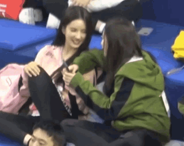 two women are sitting next to each other on a couch and one of them is holding a cell phone .