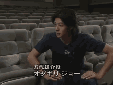 a man in a blue shirt is sitting in a row of empty seats
