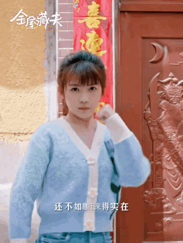 a woman in a blue sweater is standing in front of a red door