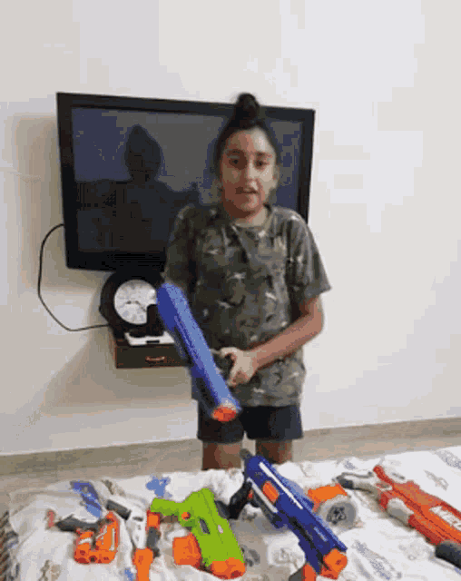 a little girl holding a nerf gun in front of a television