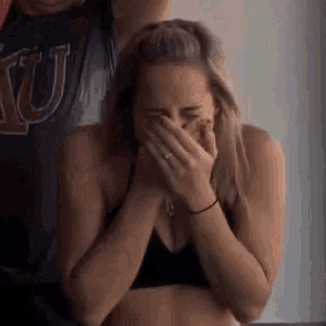 a woman in a black bra is covering her mouth with her hands while laughing .