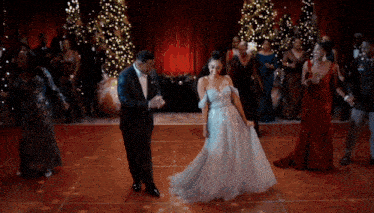 a bride and groom are dancing in front of christmas trees