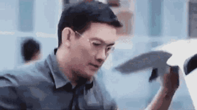 a man wearing glasses is holding a piece of paper in his hand and looking at it .