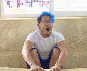 a man with blue hair and glasses is sitting on a couch with his mouth open