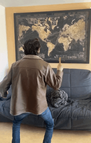 a man in a brown leather jacket is pointing at a map of the world