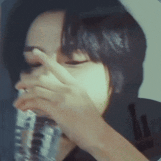a woman covering her face with her hand while drinking from a glass