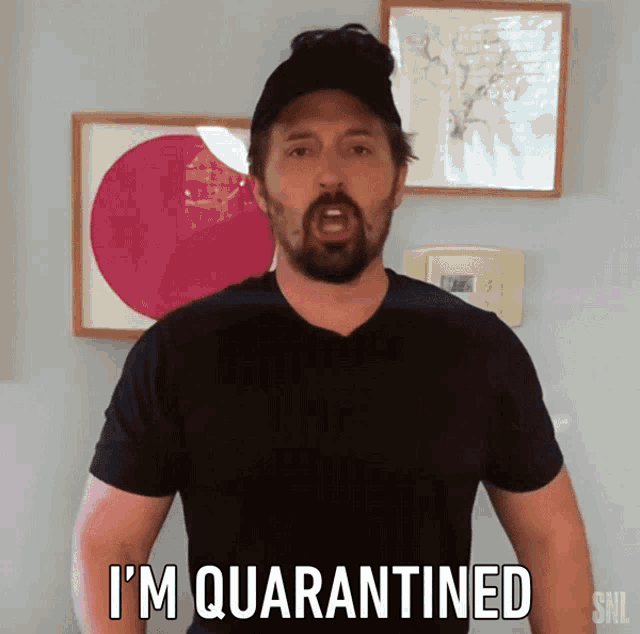 a man in a black shirt says i 'm quarantined in front of framed pictures