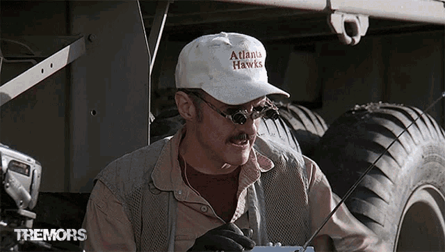 a man wearing a hat that says atlanta hawks is working on a vehicle