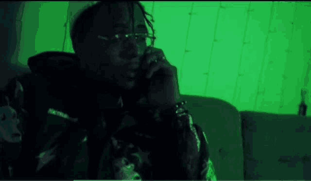 a man is sitting on a couch talking on a cell phone in a green room .