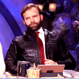 a man in a leather jacket and tie is sitting at a table with a tablet
