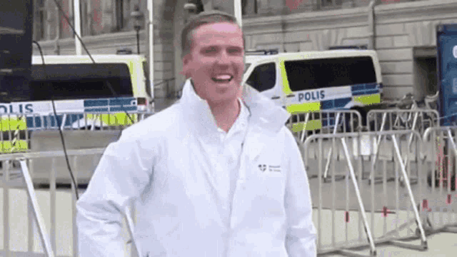 a man in a white jacket stands in front of a police van that says polis