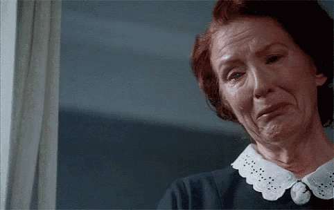 an elderly woman is crying while looking out of a window .