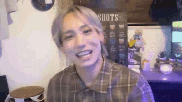a man in a plaid shirt is smiling in front of a sign that says shots .