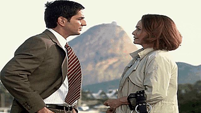 a man and a woman are looking at each other with mountains in the background
