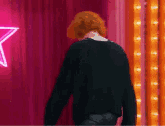 a man with red hair is standing in front of a pink curtain with a neon star in the background .