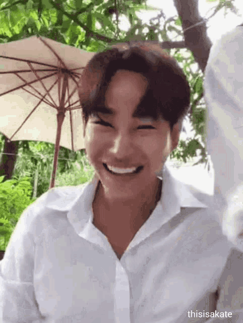 a young man in a white shirt is smiling in front of an umbrella