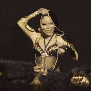 a woman in a black and gold outfit is holding a mask