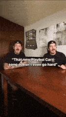 two men are sitting at a table and one of them says " that new playboi carti song doesn 't even go hard "