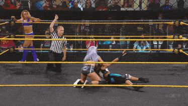 a woman with purple hair is wrestling another woman in a wrestling ring with a sign that says nxt in the background