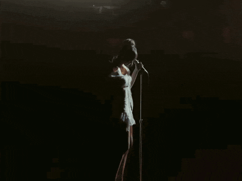 a woman stands in front of a microphone in a dark room