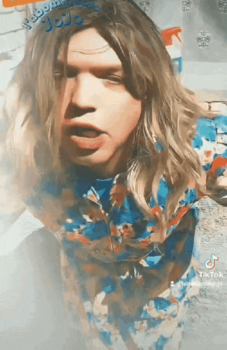 a man with long blonde hair is wearing a blue shirt with a floral pattern