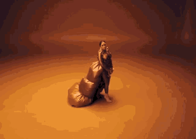 a woman in a long gold dress is standing on a pile of gold balloons .