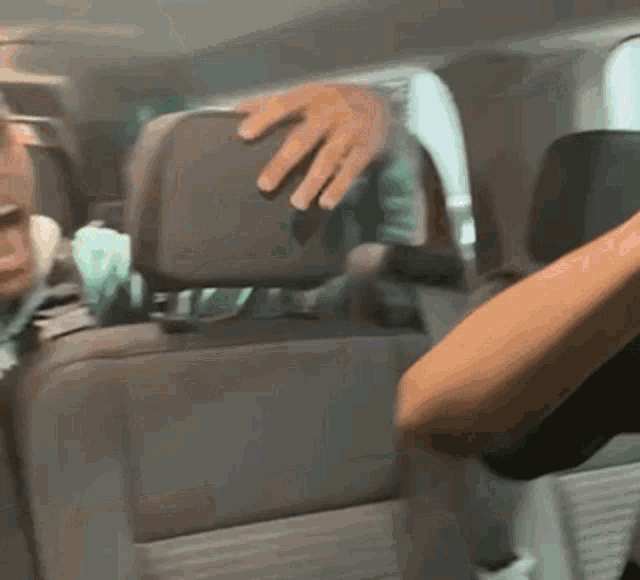 a man is putting his hand on the headrest of a car .