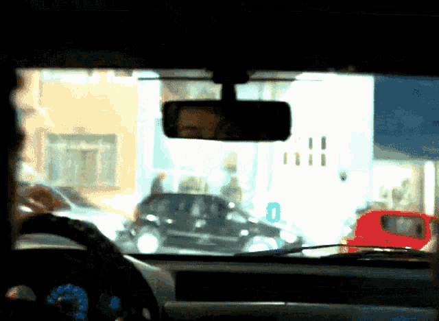 a man is driving a car and the rear view mirror shows a red van in the distance
