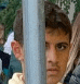 a man is behind a fence looking through a metal pole .