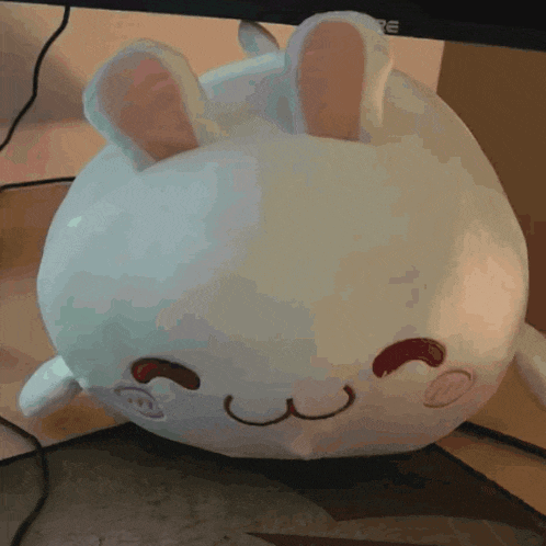 a white stuffed animal with a smiley face is sitting on a desk in front of a dell monitor