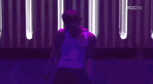a man in a purple tank top is standing on a pole in front of a purple background .