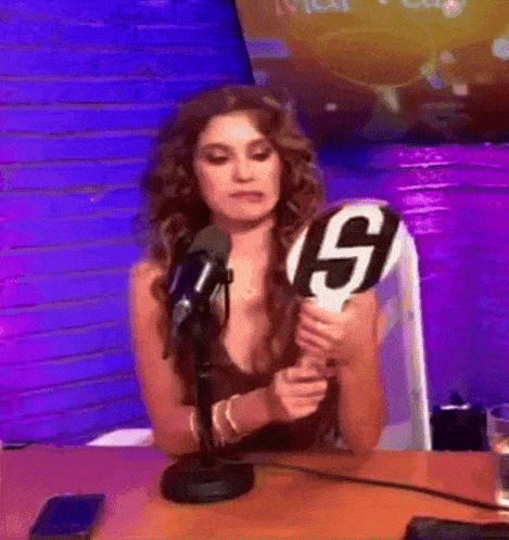 a woman is sitting in front of a microphone holding a sign that says s