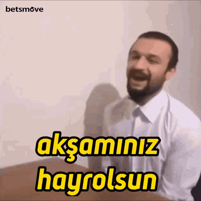 a man with a beard is sitting at a table with the words aksaminiz hayrolsun written above him