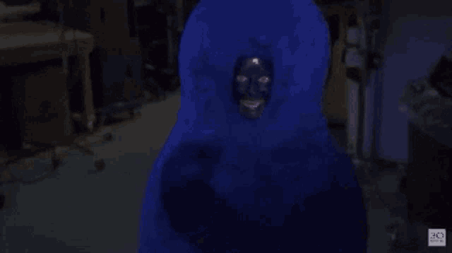a blue stuffed animal with a black face is standing in a dark room ..