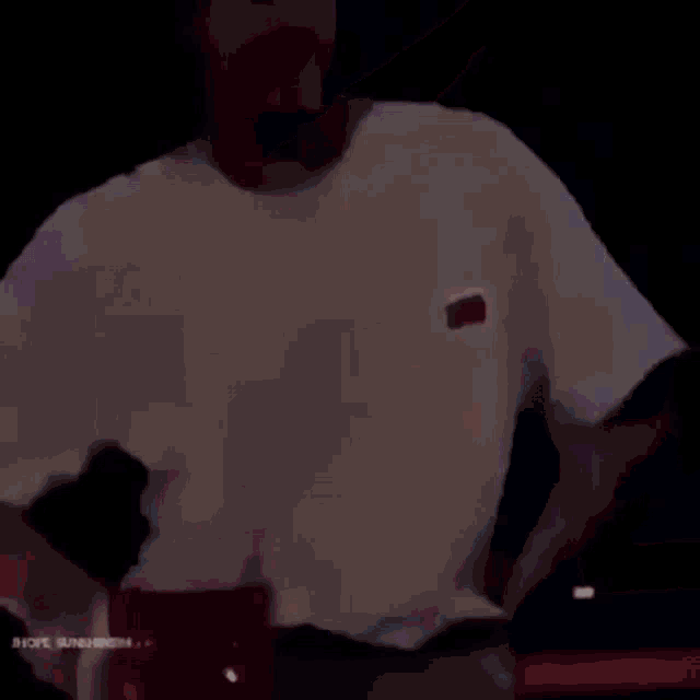 a man in a white shirt is standing in a dark room holding a red bag .