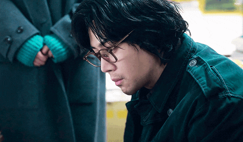 a man wearing glasses and a green jacket looks down at something
