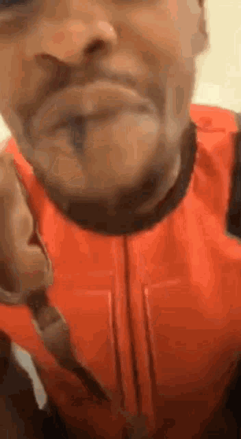 a man with a beard is wearing an orange vest and making a face .