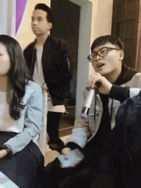 a man with glasses is singing into a microphone while sitting at a table with other people .
