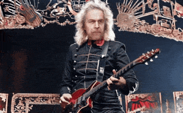 a man with blonde hair is playing a red guitar in front of a stage