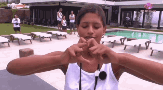 a woman is making a heart shape with her hands in front of a big brother house