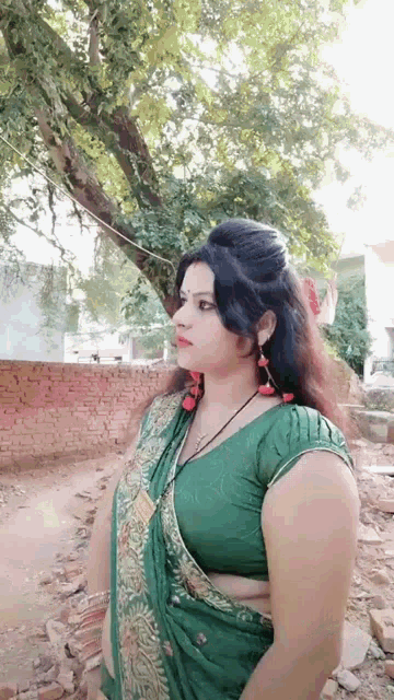 a woman in a green saree is standing in front of a tree .