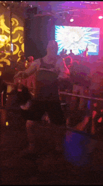 a man is dancing in a dark room with a large screen behind him