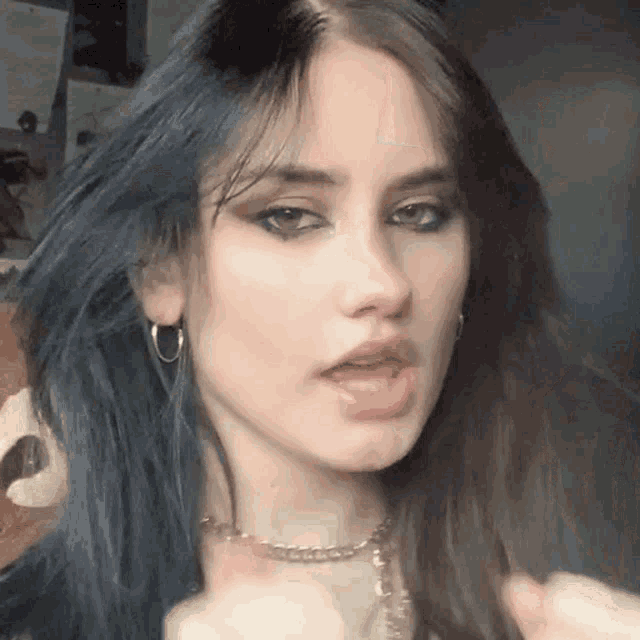 a close up of a woman 's face with blue hair wearing a choker and earrings .