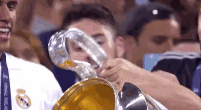 a man is drinking from a glass while holding a trophy in front of a crowd .