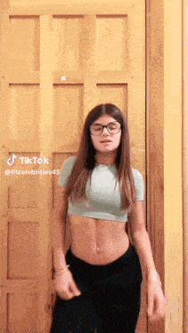 a woman wearing glasses is standing in front of a wooden door .