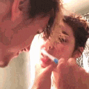 a woman is brushing her teeth in front of a mirror while a man looks on .